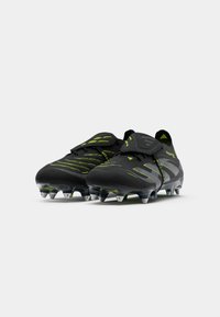Black soccer cleats with green accents, textured upper, low-profile design, and molded studs for traction. Velcro strap across the top.