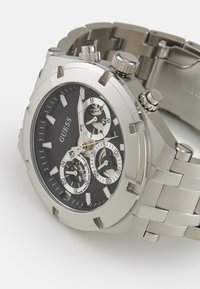 Orologio cronografo in acciaio inox argento con quadrante nero, subquadranti bianchi e indici luminosi. Dotato di bracciale metallico e ghiera testurizzata.