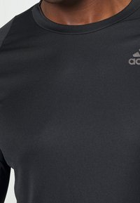 Camiseta atlética negra hecha de tejido suave, con cuello redondo, manga corta y un logotipo sutil en la parte superior derecha.