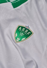 Witte sporttrui met een groen schildlogo waarin "ASSE" en "SAINT-ETIENNE" staan, omrand met gouden accenten en een blauwe ster bovenaan.