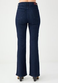 Jean évasé bleu foncé à taille haute, grandes poches arrière et texture en denim lisse. Présente des coutures discrètes et une ceinture de marque.