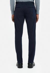 Marineblauwe broek met een rechte pasvorm, voorzien van twee achterzakken met klep en een gladde textuur, gedragen met zwarte geklede schoenen.
