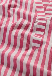 Tessuto a strisce rosse e bianche con una consistenza morbida. Presenta un collo a V e una toppa con motivi a strisce alternate.