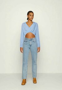 Camisa curta azul clara com decote em V, combinada com jeans de ganga claros de cintura alta e botins castanhos de salto chunky.