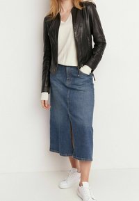 Svart läderjacka över en ljus tröja, kombinerad med en knälång jeanskjol med en slits fram och vita sneakers.