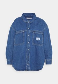 Sininen farkkupaita pitkällä hihalla, nappikiinnitys edessä, kaksi rintataskua ja pieni Calvin Kleinin logopatch oikeassa taskussa.