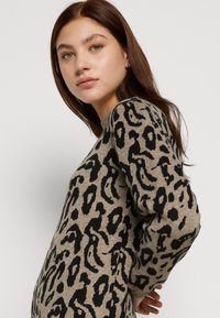 Beige trui met luipaardprint, voorzien van zwarte patronen, lange mouwen, ronde halslijn en een zachte textuur.