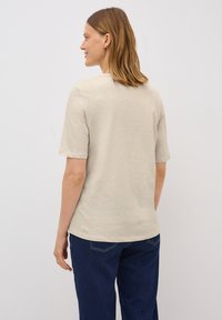 Beige top s krátkým rukávem a kulatým výstřihem, hladkou texturou a volným střihem. Vybaven tmavě modrými džíny s zadními kapsami.