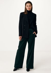 Svart dubbelkn�äppt blazer över en åtsittande svart polotröja, kombinerad med vida mörkgröna kordbyxor och svarta spetsiga klackskor.