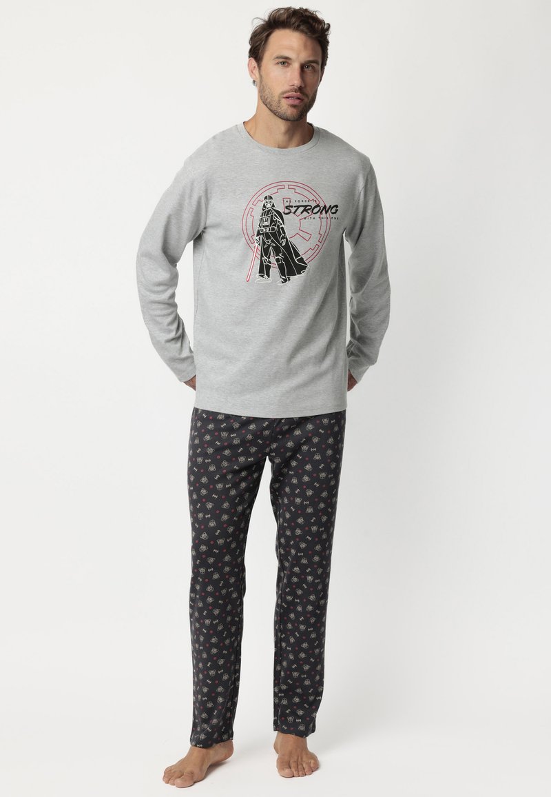 Camisa de manga larga gris con diseño gráfico en negro y rojo; combinada con pantalones de pijama negros que tienen pequeños patrones coloridos. Tejido de algodón suave.