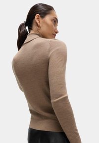 Beżowy sweter z długim rękawem o kołnierzykowym designie, z prążkowanymi mankietami i gładką teksturą, posiadający widoczne detale szwów na ramionach.