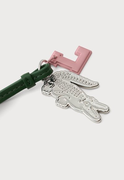 Sangle en cuir vert avec deux porte-clés métalliques attachés : une clé rose en forme de L et un pendentif argenté en forme de crocodile.