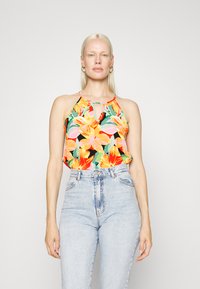 Top halter floral com um vibrante padrão de cores mistas, apresentando flores laranjas e cor-de-rosa sobre um fundo preto, combinado com jeans de cintura alta azul claro.