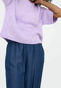 Maglione a maniche corte in lilla lavorato a maglia con texture a coste, abbinato a pantaloni larghi in denim scuro con cintura elastica.