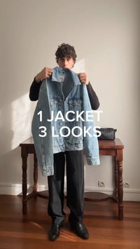 Muž drží svetlomodrú denimovú bundu pred sebou, stojí v interiéri pri drevenom stole s čiernou pletenou taškou. Text znie "1 bunda 3 štýly."