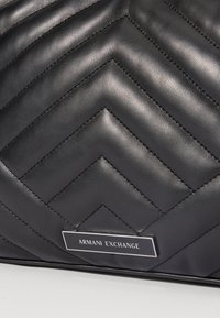 Czarna pikowana skórzana torba z motywem w zygzak i metalową tabliczką z logo. Charakteryzuje się gładką fakturą i eleganckim designem. Idealna na różne okazje.