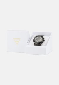Reloj de acero inoxidable negro con esfera redonda, múltiples diales y un bisel negro, presentado en una caja blanca de marca con acentos dorados.