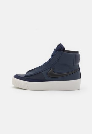 Wysokie granatowe trampki z czarnym logo typu swoosh i białą gumową podeszwą, pokazane z boku na jednolitym tle.