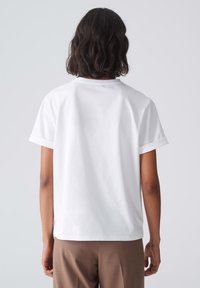 T-shirt blanc à manches courtes avec un col rond et une coupe décontractée, fabriqué en coton, présentant des manches à revers et un ourlet droit.