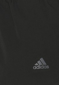 Svarta sportshorts i mjukt tyg, med elastisk midja och en diskret grå Adidas-logotyp på nedre vänstra sida.