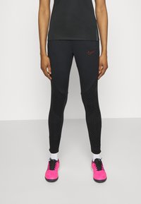 Czarne legginsy sportowe z akcentami w geometryczny wzór, połączone z jasnoróżowymi butami i czarną bluzką z okrągłym dekoltem.