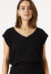 Schwarzes Textiltop mit V-Ausschnitt, kurzen Ärmelchen und lockerer Passform. Der Stoff zeigt ein gekrepptes Muster und ist mit einem Kordelzugbund ausgestattet.