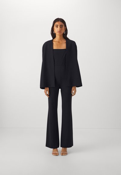 Jumpsuit nero strutturato con pantaloni a gamba larga, scollatura quadrata e un mantello fluido coordinato. Tessuto liscio e sartoriale, finitura elegante.