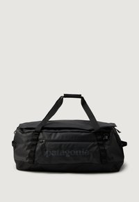 Sort Patagonia duffel bag med dobbel topgreb, frontlomme med lynlås og minimalistisk design på en lys ensfarvet baggrund.