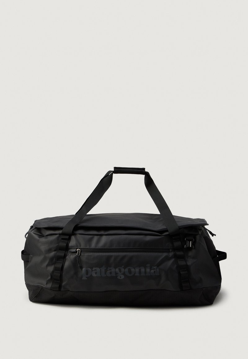 Sort Patagonia duffel bag med dobbel topgreb, frontlomme med lynlås og minimalistisk design på en lys ensfarvet baggrund.