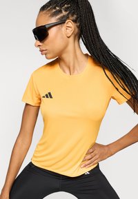 Short-sleeved, fitted yellow athletic shirt with a smooth texture and a black logo accent. Paired with black athletic leggings.