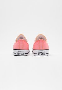 Różowe trampki z płóciennego materiału o niskim profilu. Posiadają białe gumowe podeszwy i czarne paski, z logo "CONVERSE ALL STAR" na pięcie.