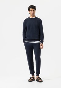 Navyblauwe sweater met een ronde hals, gecombineerd met bijpassende tapering broek en zwarte sandalen met een decoratieve band. Soepele textuur.