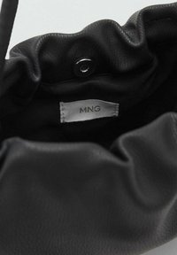 Svart läderdragsäck med en mjuk yta. Inre etikett med texten "MNG." Har ett tryckknappsstängning och samlad toppdesign.