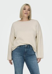Pull en crème avec une texture douce, à coupe décontractée et encolure large, associé à un jean en denim bleu clair. Tissu doux et douillet avec de longues manches.