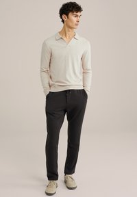 Polo de culoare bej deschis, cu mâneci lungi și guler tăiat, asociat cu pantaloni negri și adidași bej. Textură netedă, croială casual.