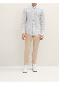 Lichtblauw overhemd met witte streepjes, gecombineerd met beige broeken en witte sneakers. Het overhemd heeft een ronde zoom en donkere knopen.