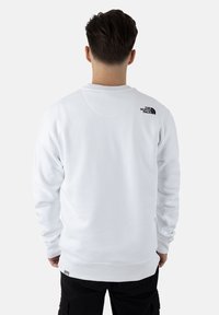 Sudadera blanca con cuello redondo y mangas largas. Presenta un pequeño logo negro en la parte superior de la espalda. Textura suave y lisa.