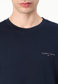 Marineblå crew-neck t-skjorte laget av bomull, med en liten "TOMMY JEANS" logo på venstre brystområde med hvite og røde detaljer.