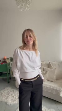 Top bianco scollato con orlo costellato, abbinato a pantaloni neri a vita alta e cintura metallica. Tessuto leggero e strutturato.