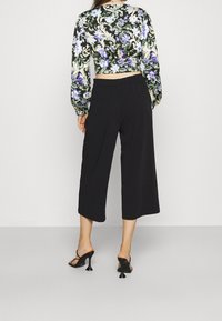 Pantaloni neri a 3/4 con una texture liscia, dotati di una vita e un taglio dritto. Abbinati a una maglia floreale a maniche lunghe e tacchi con cinghie.