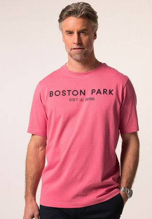 Růžové bavlněné tričko s krátkým rukávem a klasickým výstřihem. Na hrudi má nápis "BOSTON PARK EST 1996" tištěný v černé barvě.