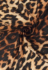 Tessuto con stampa leopardata caratterizzato da macchie nere su uno sfondo beige, con una texture morbida, arrotolato a spirale. Nome del marchio visibile: Guess.