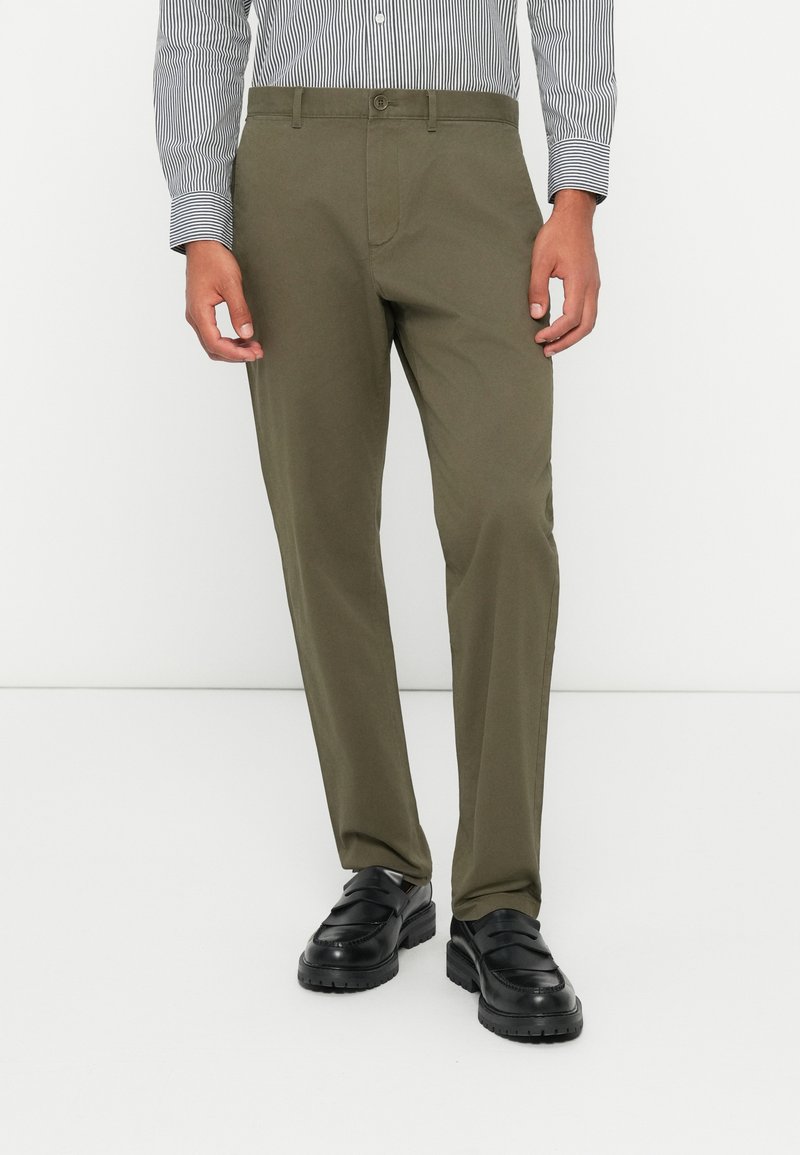 Olive green, straight-fit trousers made of lightweight fabric. Features a buttoned waistband and two side pockets. Black shoes complete the look.