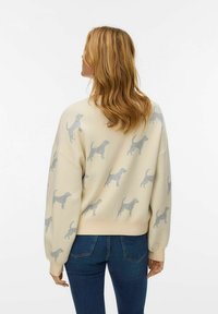 Creme sweatshirts med et dekorativt mønster af grå hunde, afslappet pasform, ribbede manchetter og kant. Båret med blå jeans.