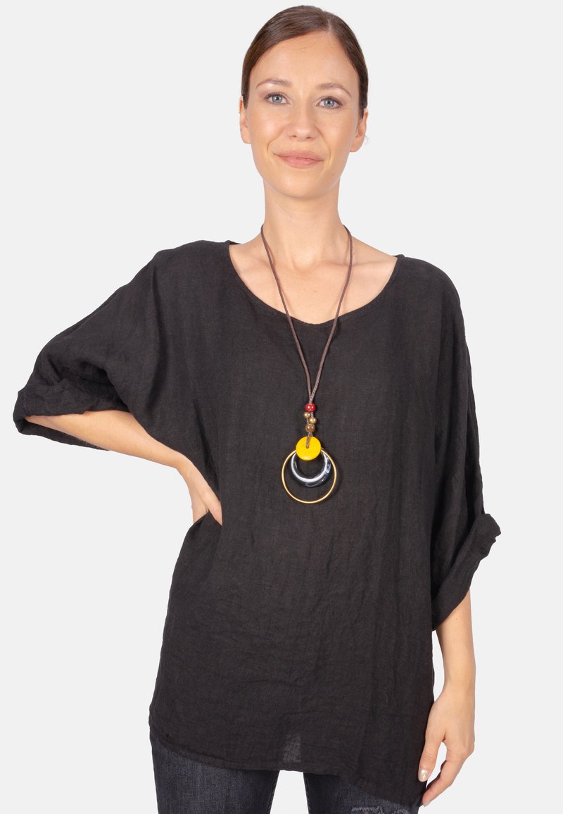 Schwarze Leinenbluse mit lässiger Passform und aufgerollten Ärmeln. Sie verfügt über eine kreisförmige, mehrfarbige Halskette mit gelben, schwarzen und goldenen Akzenten.