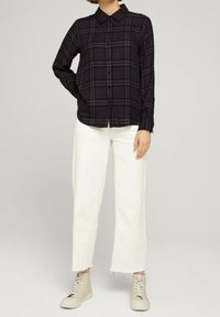 Svart och grå rutigt knäppskjorta med långa ärmar, kombinerad med vita vida byxor och ljusbeiga hög-top sneakers.