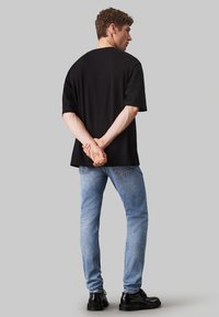 Czarna bawełniana koszulka, luźny krój, krótkie rękawy; w zestawie z jasnoniebieskimi dżinsami i czarnymi butami. Prosty design, bez widocznych wzorów.