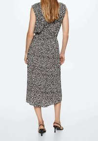 Robe midi à motifs noirs et blancs avec une coupe décontractée, sans manches, et une ceinture nouée à la taille, associée à des talons noirs à lanières.