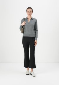 Pullover grigio a maglia con colletto, pantaloni neri a campana e scarpe grigie slip-on. Il modello tiene una piccola borsa a mano di colore oliva.