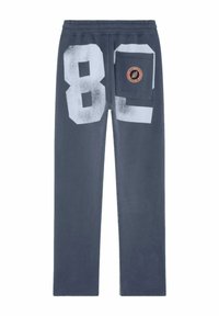Pantalon de survêtement gris avec une finition texturée, présentant de grands chiffres blancs "80" au dos et une poche latérale avec un patch logo.